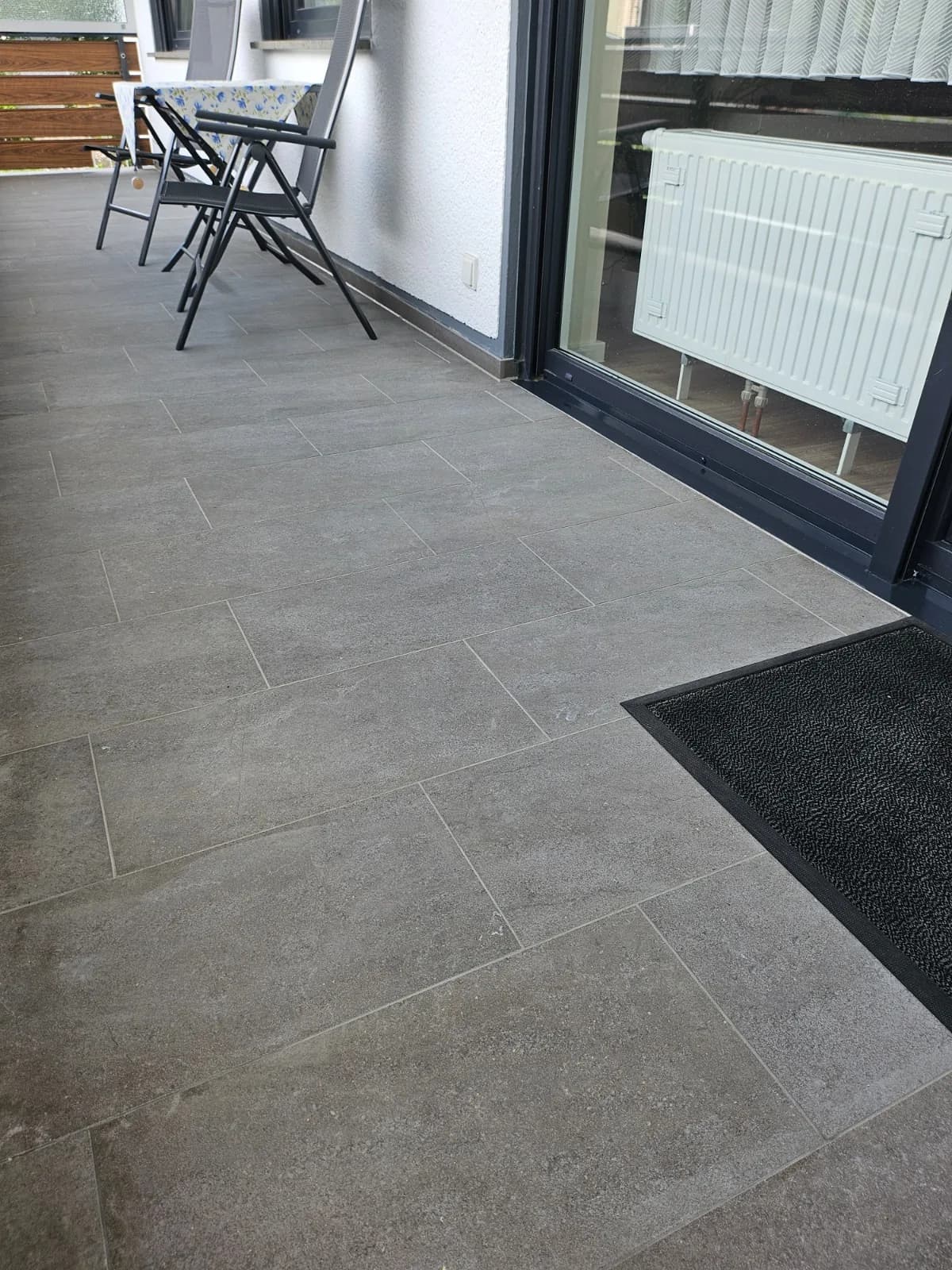 Fertig sanierter Balkon mit neuem grauen Fliesenboden vor der Terrassentür
