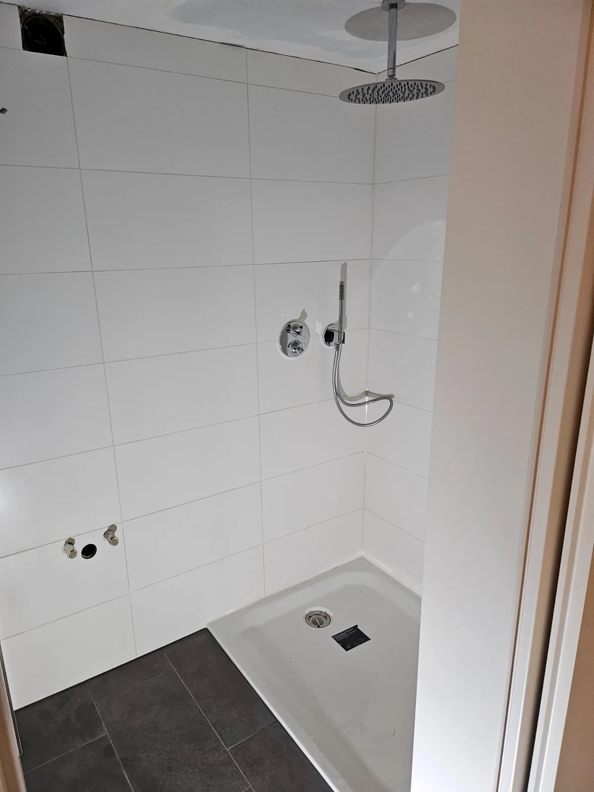 Fertiges Badezimmer mit bodengleicher Dusche, weißen Wandfliesen und dunklem Fliesenboden