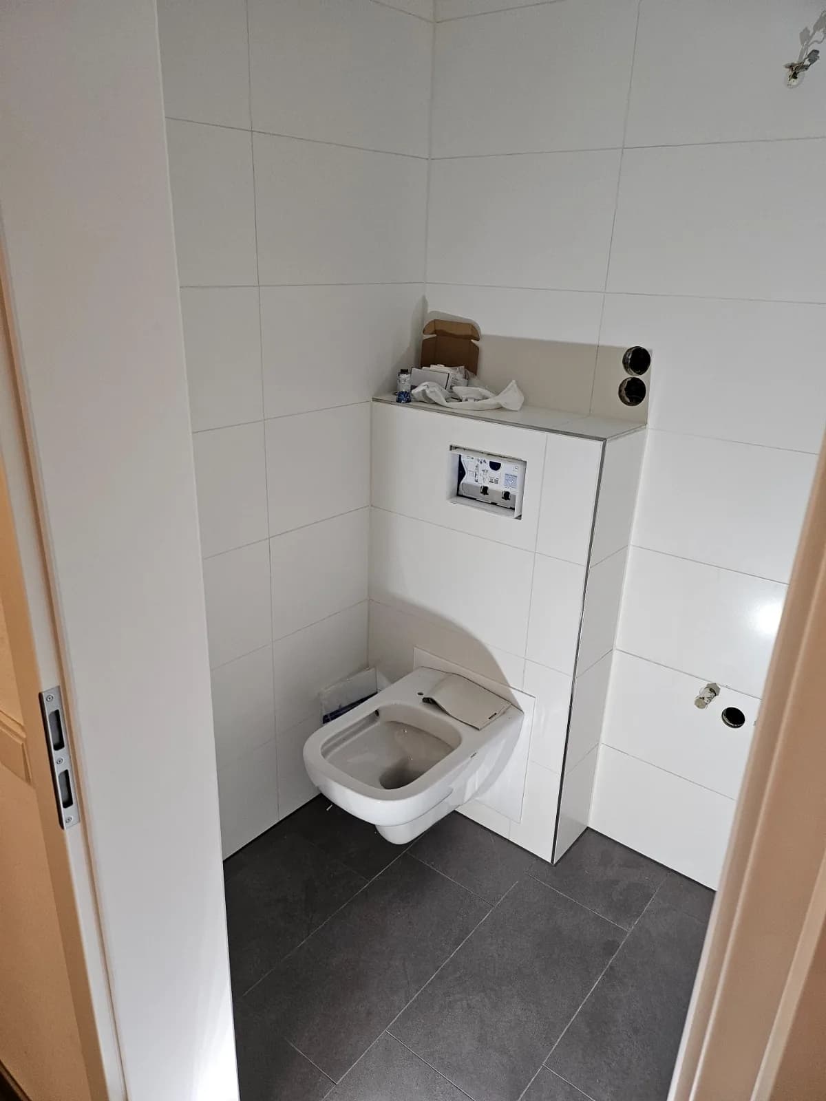Badezimmer mit wandhängendem WC vor Vorwandinstallation und dunklem Fliesenboden