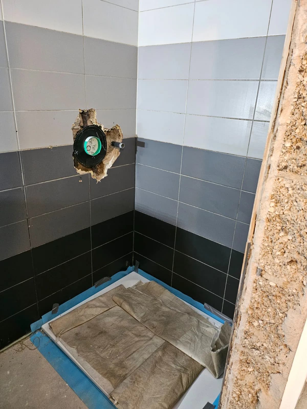 Badezimmer im Rückbau mit alten Wandfliesen und abgedecktem Boden
